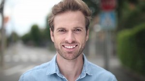 camera closing in to a young man standing with a big smile on his face and looking ahead