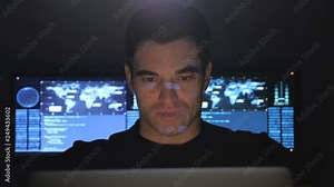 Portrait of developer programmer working on computer in a data center filled with monitor screens. Binary code on his face