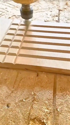 CNC router bit carving repetitive stepped trench patterns into a light wood board